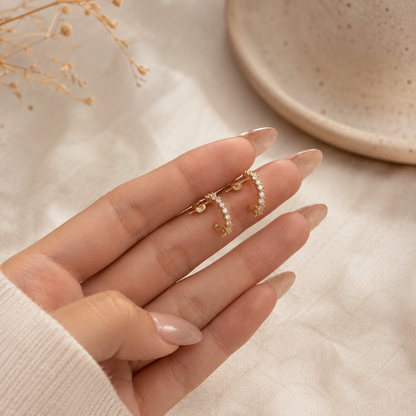 Goldene Celestia Ohrringe mit funkelndem Steinbesatz als Detailaufnahme in der Hand