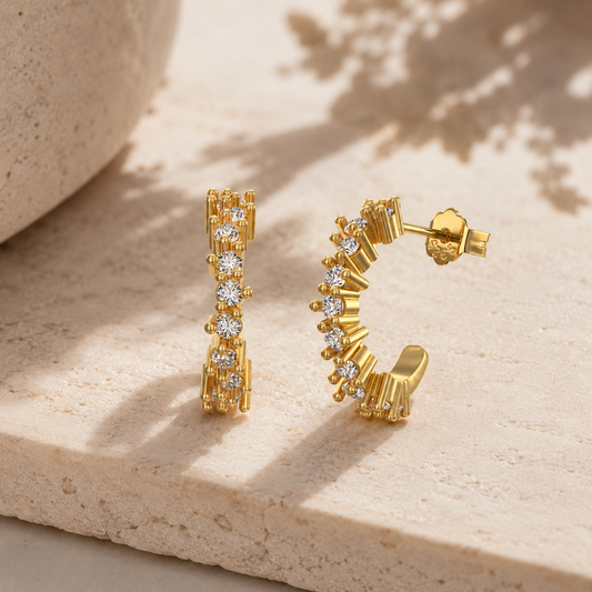 Goldene Celestia Ohrringe mit halbkreisförmigem Design und funkelnden Steinen auf hellem Marmor